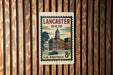 A vintage postage stamp from the United States of America, featuring an illustration of a town with a clock tower, hanging on a wooden wall.