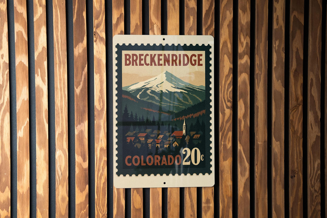 A vintage-style metal sign with a mountain landscape and a small town in the background, mounted on a wooden wall.