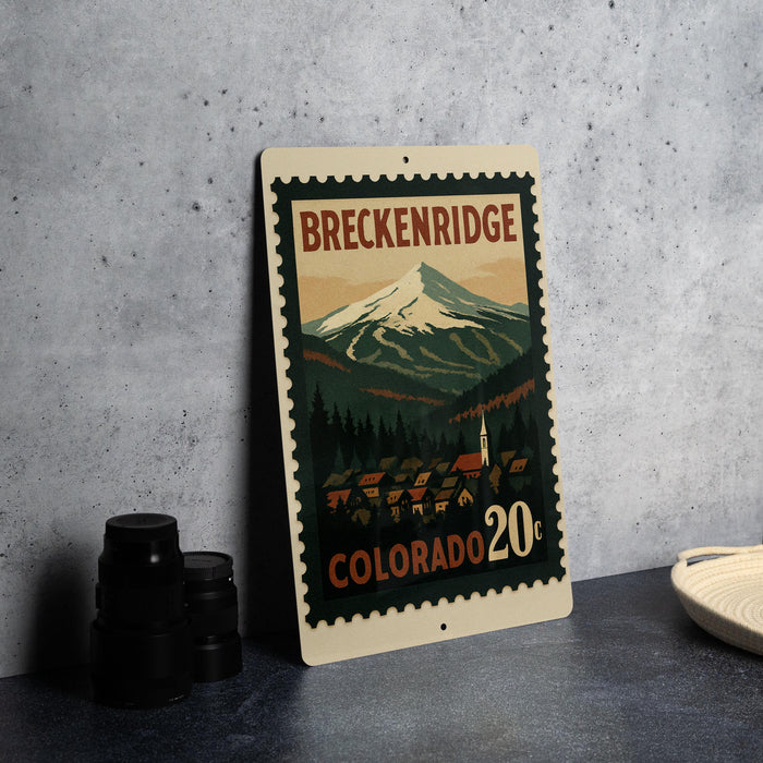A metal sign with a mountain landscape and a small town in the background, featuring the text "BREKENRIDGE COLORADO 20¢".
