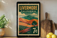 A vintage-style poster of Livermore, California, featuring a landscape with rolling hills and mountains, is displayed on a wall next to a wooden cutting board and a potted plant.
