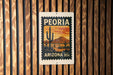 A vintage-style postage stamp from Arizona, featuring a desert landscape with cacti and mountains, is displayed on a wooden wall.