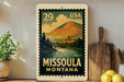 A vintage-style metal stamp depicting a scenic landscape of Missoula, Montana, with a mountain, river, and town in the background.