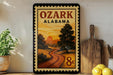 A framed poster of a scenic landscape with a winding road and a sunset in the background, displayed on a wall next to a wooden cutting board and some potted plants.