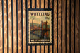 A vintage postage stamp from West Virginia, featuring a bridge and a river, is displayed on a wooden wall.