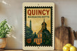 a framed poster of QuINCY, Massachusetts, with a depiction of the state's iconic dome and buildings.