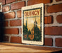 A vintage-style metal sign with the text "QUINCY MASSACHUSETTS" displayed on a brick wall.
