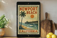 A framed poster of Newport Beach, California, featuring a palm tree and a wooden pier, is displayed on a shelf next to a wooden cutting board and a potted plant.