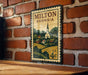 A vintage postage stamp from Milton, Georgia, featuring a church and a rural landscape, is displayed on a brick wall.