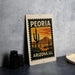 A metal sign with a desert landscape and cacti design, featuring the text "PEORIA ARIZONA 20¢" on it.