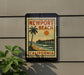 A vintage-style sign for Newport Beach, California, featuring a palm tree and a pier, mounted on a wall.