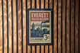 A vintage-style postage stamp from Everett, Washington, mounted on a wooden wall.