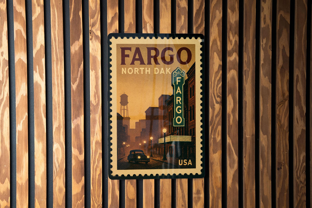 A framed poster of a city street with a car and a sign for the Fargo theater, mounted on a wooden wall.