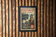 A vintage postage stamp from New Jersey featuring a building with a clock tower and a tree, mounted on a wooden wall.