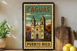 A vintage-style sign for Cagua, Puerto Rico, featuring an illustration of a church with two towers and palm trees, is displayed on a shelf next to a wooden cutting board and a potted plant.