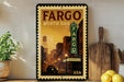 a framed poster of a cityscape with a vintage-style sign for the Fargo, North Dakota theater, displayed on a shelf next to a wooden cutting board and some lemons.