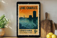 A framed vintage postage stamp depicting Lake Charles, Louisiana, with a silhouette of the city skyline and a body of water in the background.