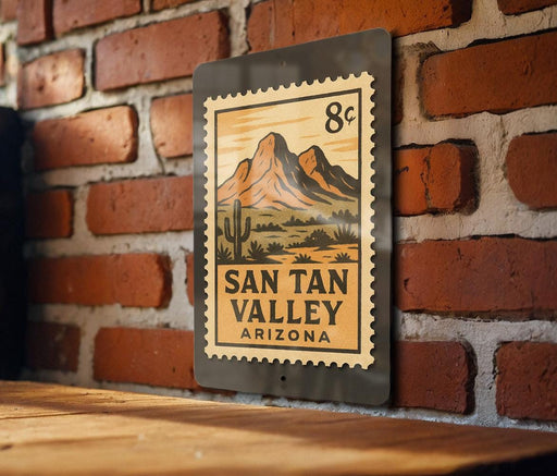 A metal sign with a desert landscape and mountains, mounted on a brick wall.