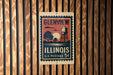 A vintage postage stamp from the United States of America, featuring a water tower and trees, is displayed on a wooden wall.