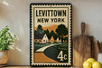A framed poster of Levitown, New York, with a vintage-style illustration of houses and a road, displayed on a shelf next to a wooden cutting board and some lemons.