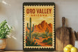 A framed poster of the Oro Valley in Arizona, featuring a desert landscape with cacti and mountains in the background.