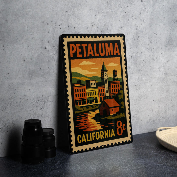 A vintage-style metal stamp depicting a cityscape with a clock tower, placed on a countertop next to some black camera lenses.