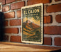 A vintage-style postage stamp from California, featuring a mountain landscape, is displayed on a brick wall.