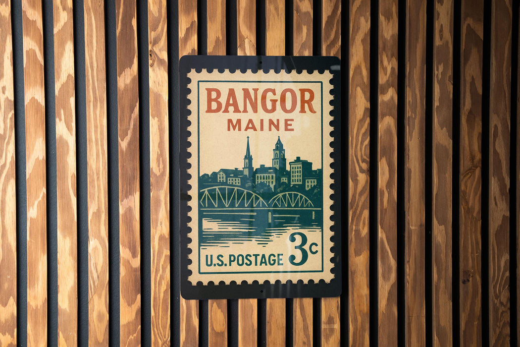 A vintage postage stamp from Bangor, Maine, featuring a cityscape and a bridge, is displayed on a wooden wall.