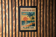 A vintage-style postage stamp from Florida, featuring a palm tree and sunset, is displayed on a wooden wall.
