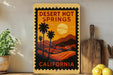 A vintage-style metal sign for Desert Hot Springs, California, featuring a palm tree and sunset landscape.