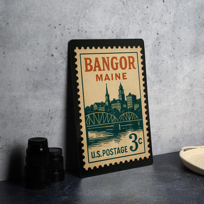 A vintage postage stamp from Maine, featuring a cityscape and a bridge, is displayed on a table.