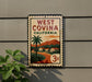 A vintage-style West Covina, California postage stamp is displayed on a wall, with a plant in the foreground.