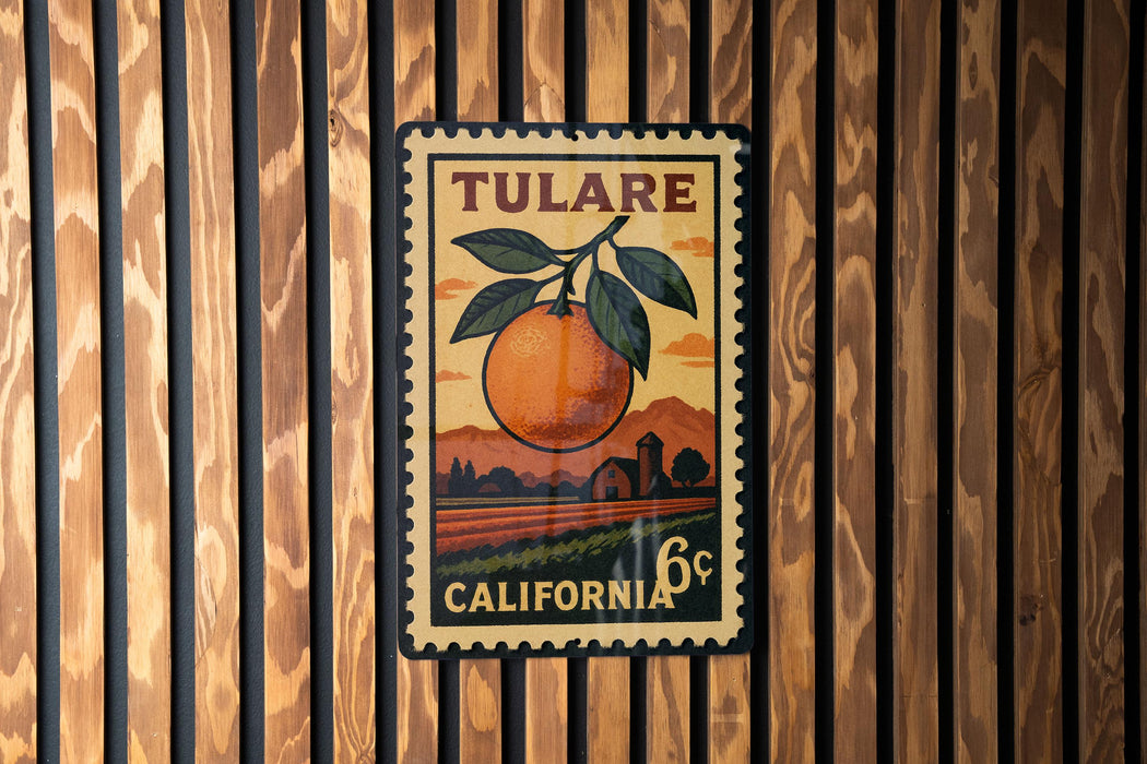 A vintage postage stamp from Tulare, California, featuring an orange and a leaf, is displayed on a wooden wall.