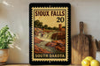 A framed vintage-style poster of Iowa Falls, featuring a waterfall and a building, is displayed on a shelf next to a wooden cutting board and a potted plant.