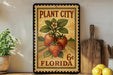 A vintage-style metal sign advertising "Plant City Florida" with a strawberry illustration, placed on a wooden shelf next to a potted plant and a wooden cutting board.