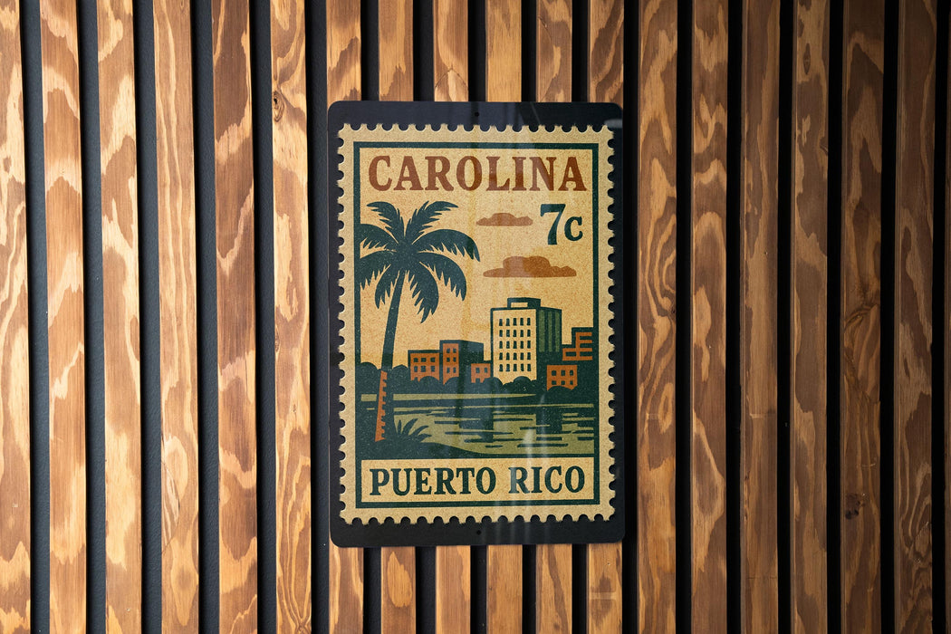 A vintage-style postage stamp from Carolina, featuring a palm tree and buildings, is displayed on a wooden wall.