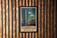 A vintage-style postage stamp from the United States, featuring the name 'Ferndale' and the location 'Michigan', hanging on a wooden wall.