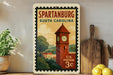 A vintage postage stamp depicting a clock tower in Spartanburg, South Carolina, with a wooden post and a wooden cutting board in the foreground.