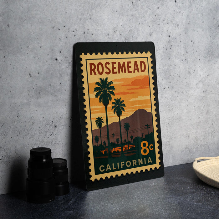 A framed vintage postage stamp from California, featuring a sunset scene with palm trees and mountains, is displayed on a table.