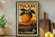 A vintage-style metal sign with an illustration of an orange and a rural landscape, mounted on a wall next to a wooden cutting board and some kitchen utensils.