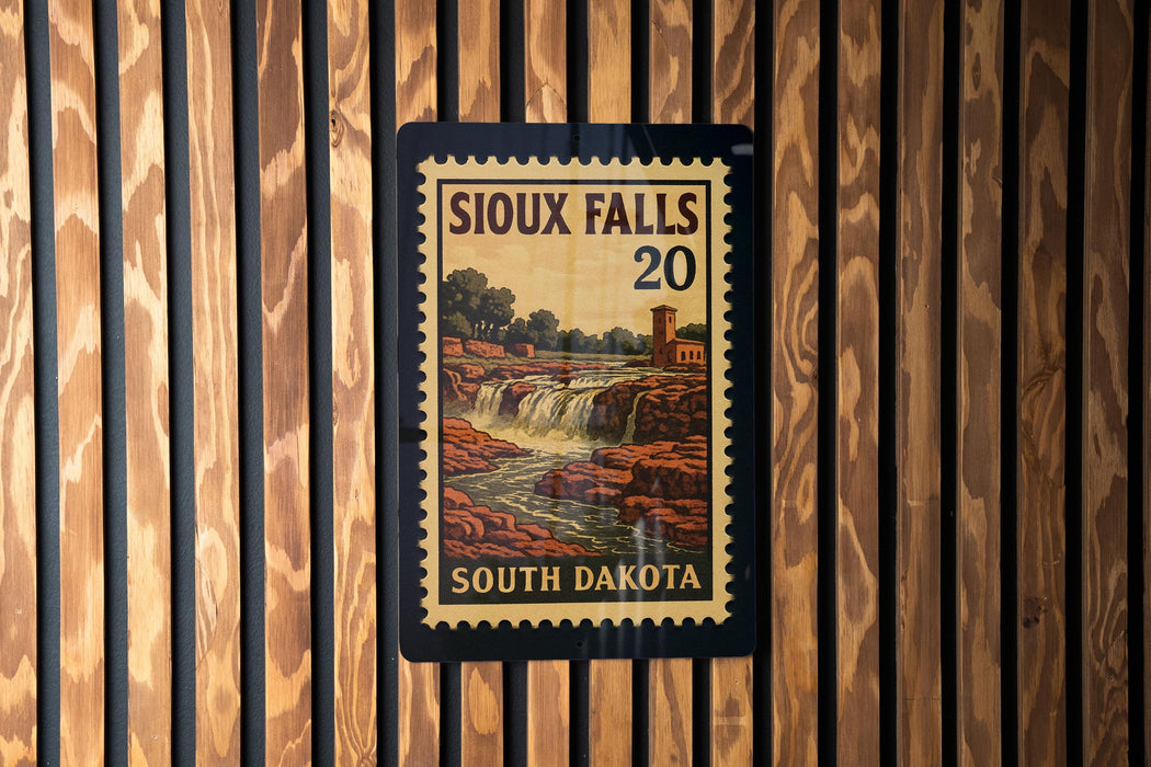 A framed poster of the scenic falls in South Dakota, featuring a waterfall and a building, is displayed on a wooden wall.