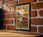 A vintage-style postage stamp depicting the scenic falls of Sioux Falls, South Dakota, hanging on a brick wall.