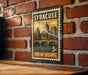 A vintage postage stamp from New York, featuring a cityscape and a bridge, is displayed on a brick wall.