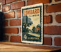 A vintage postage stamp from the United States of America, featuring an illustration of a rural scene with a house and trees, mounted on a brick wall.