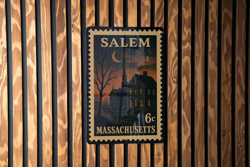 A framed Massachusetts postage stamp depicting a house and a church, mounted on a wooden wall.