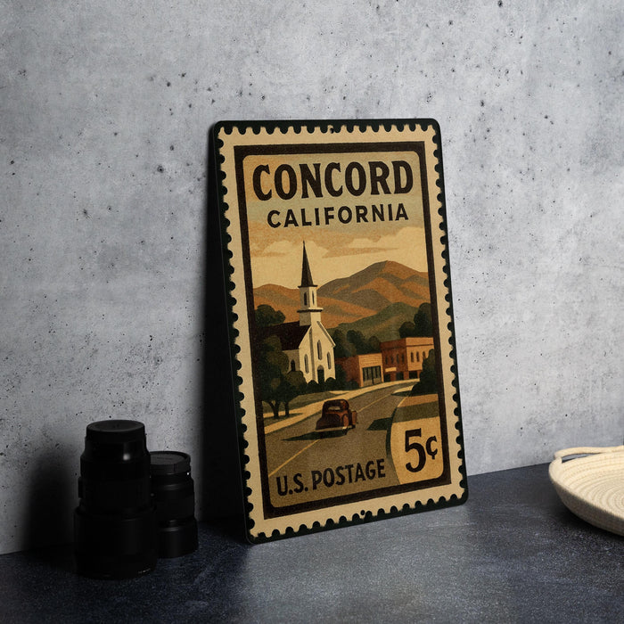 A vintage Concord, California postage stamp with a church and mountains in the background, sitting on a table next to some black camera lenses.