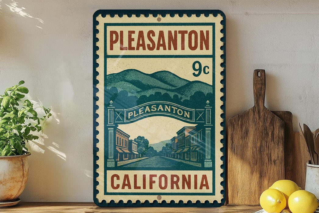 A vintage-style metal sign with the text "PLEASANTON 9c" and an illustration of a small town, with the text "CALIFORNIA" below it. The sign is displayed on a shelf next to a wooden cutting board and a potted plant.