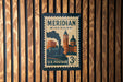 A vintage-style postage stamp from the United States, featuring an illustration of a train and buildings, mounted on a wooden wall.