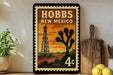 A vintage-style stamp depicting a desert scene with a tower, a cactus, and a sunset, along with the text "HOBBS NEW MEXICO" and a denomination of 4 cents.