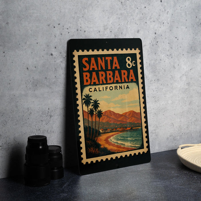 A vintage-style metal sign with a beach scene and mountains in the background, featuring the text "SANTA BARBARA CALIFORNIA" and a postage stamp design.