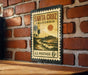 A vintage-style postage stamp from the United States, featuring a beach scene with palm trees and a sunset, mounted on a brick wall.
